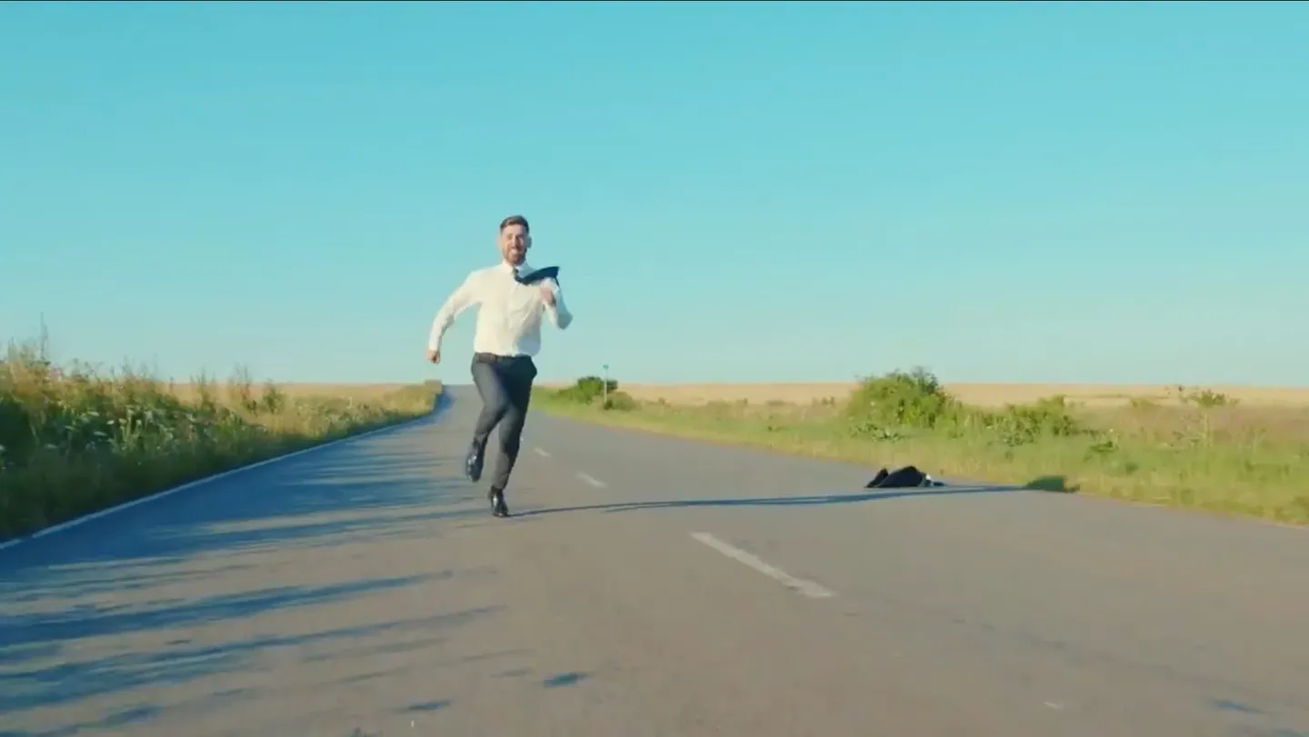 A man in business attire running joyfully down an open road.